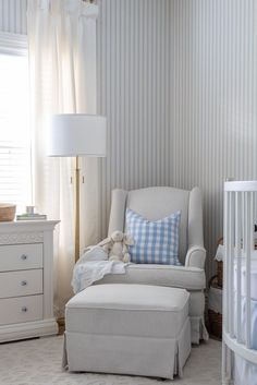 a baby's room with blue and white striped wallpaper, a chair and footstool