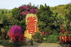 a sign that is in the middle of some bushes and trees with flowers around it