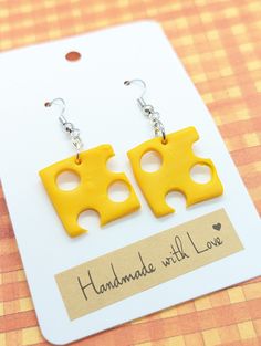 two pieces of cheese are hanging from earrings on a card with the words handmade with love