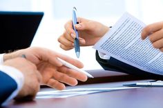 two people sitting at a table with papers and pen in their hands while another person is writing something on the paper