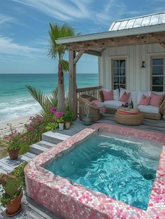 a hot tub sitting on top of a wooden deck next to the ocean in front of a house