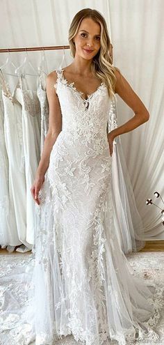 a woman in a white wedding dress standing next to some dresses hanging on a rack