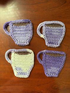 four crocheted coffee cups sitting on top of a wooden table