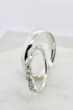 two white gold rings with diamonds on top of a marble slabd surface, one in the shape of a spiral