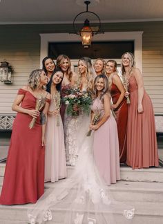 a group of women standing next to each other in front of a house wearing dresses