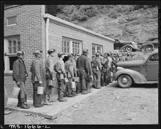 a group of men standing next to each other in front of a brick building with an old car