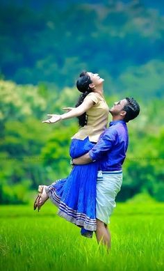 a man holding a woman in the air while standing on top of a lush green field