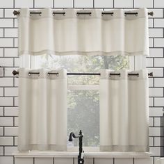 a kitchen window with white curtains and black faucet