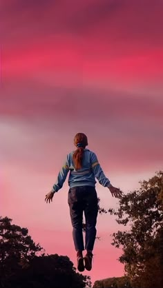 a person jumping in the air with their arms spread wide and hands outstretched, against a pink sky