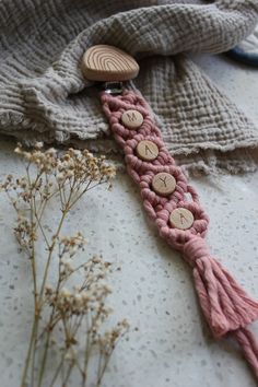 a pink crocheted tie with wooden buttons on it next to some dried flowers