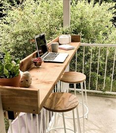 a laptop computer sitting on top of a wooden table next to two stools and a potted plant