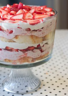 a layered cake with strawberries in it on a glass dish sitting on a polka dot tablecloth