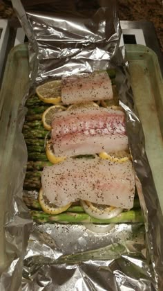 asparagus wrapped in foil with fish and lemons on top, sitting on a baking sheet