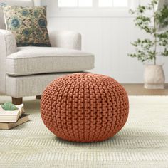 an orange knitted ball sits on the floor in front of a chair and books