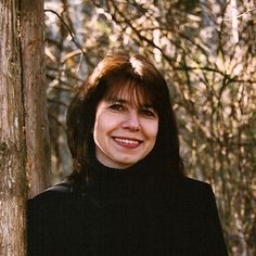 a woman standing next to a tree in the woods