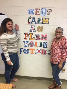 two women standing next to each other in front of a wall with letters on it