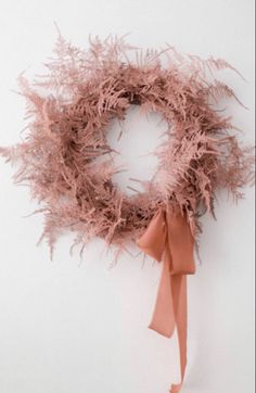 a pink wreath with an orange ribbon hanging from it's side on a white wall