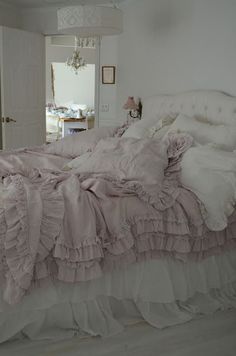 a bed with ruffled bedspread and pillows in a white room next to a doorway