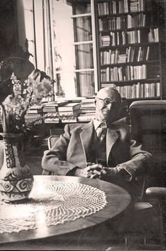 an old black and white photo of a man sitting at a table in front of a bookshelf