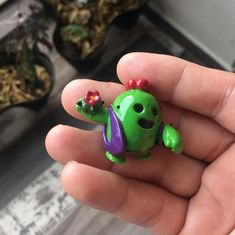 a hand holding a small green toy with flowers on it's head and eyes