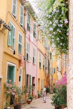 a person walking down an alley way between two buildings with green shutters on the windows