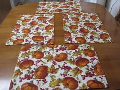 four placemats with pumpkins and berries on them sitting on a wooden table