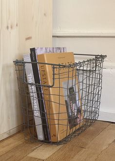 a wire basket with books in it sitting on the floor next to a wooden door