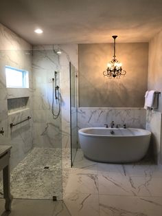 a bathroom with marble walls and flooring, a chandelier above the bathtub