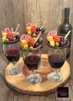 three wine glasses filled with red wine, olives and cheese on a wooden tray