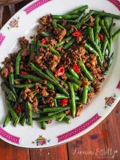 a white plate topped with green beans covered in ground beef and chili sauce on a wooden table