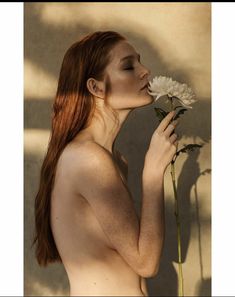 a naked woman holding a flower in her right hand and smelling it with both hands