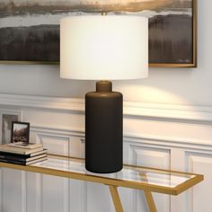 a black lamp sitting on top of a glass table next to a painting and books