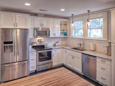 an empty kitchen with stainless steel appliances and white cabinetry, including a wood floor