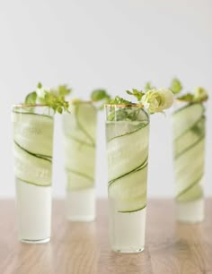 four glasses filled with cucumber and flowers on top of a wooden table next to each other