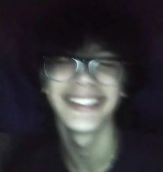 a blurry photo of a man wearing glasses and a black hat smiling at the camera