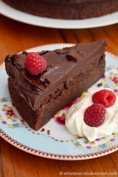 a piece of chocolate cake on a plate with whipped cream and raspberries next to it