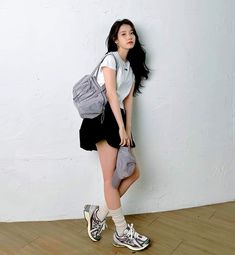 a young woman is leaning against a wall with a backpack on her shoulder and shoes on the floor