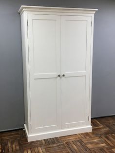 a white armoire sitting on top of a wooden floor next to a gray wall