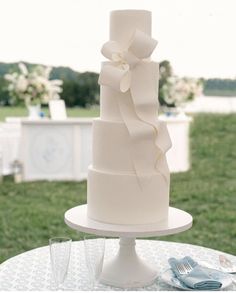 a white wedding cake sitting on top of a table next to two glasses and a fork