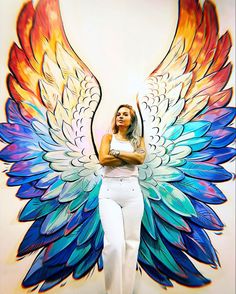 a woman standing in front of a colorful angel wings mural