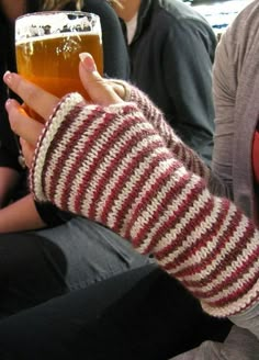 a person holding a beer in their hand while sitting on a bench with other people