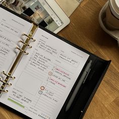 an open planner sitting on top of a wooden table next to a cup of coffee