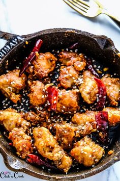 chicken with sesame seeds in a skillet next to a fork and spoon on a white table