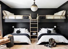 two beds in a room with black walls and white bedding, one has a ladder to the ceiling