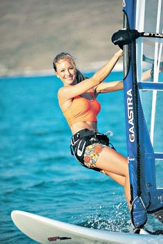 a woman on a surfboard in the water with a sailboat behind her,