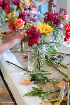 a table topped with lots of vases filled with flowers next to scissors and paper