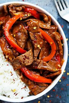 a white bowl filled with rice and meat on top of a blue table cloth next to a fork