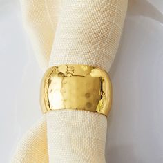 a napkin with a gold ring on top of it next to a white cloth covered napkin