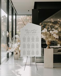 a white sign sitting on top of a floor next to vases filled with flowers