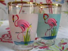 two glasses with flamingos painted on them are sitting on a tablecloth covered surface